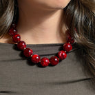 Chunky Statement-Kette mit großen, glänzenden, bordeauxroten Acrylperlen in marmorierter Optik und kleinen goldfarbenen Edelstahlperlen. Die Kette wird am Hals getragen und zu einem dunkelgrauen Oberteil kombiniert.